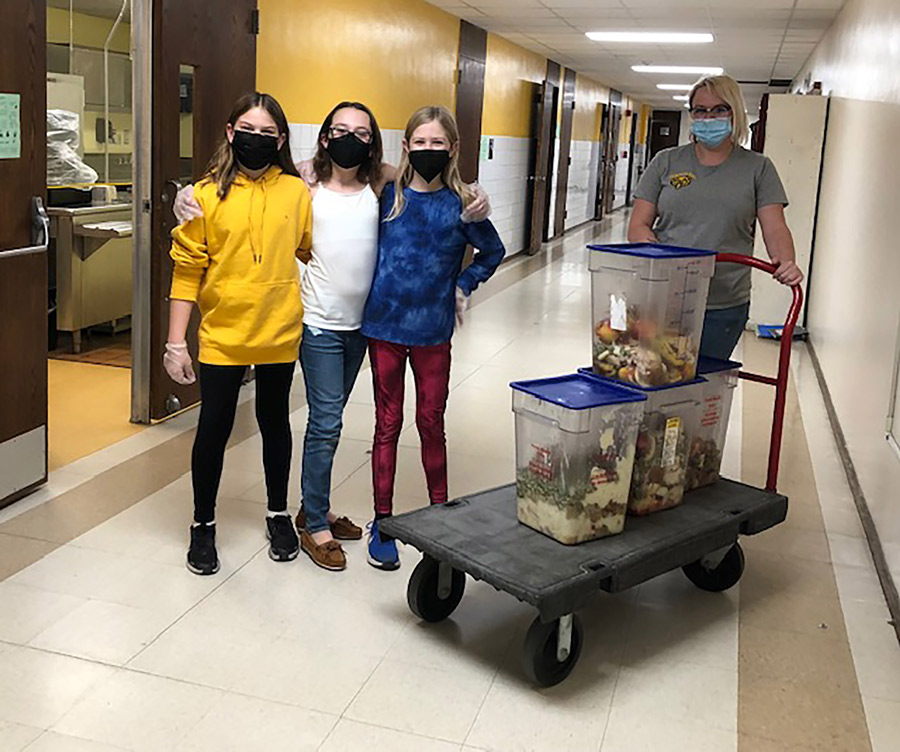 三位学生用手对着彼此站在一起 装箱里有食品废品